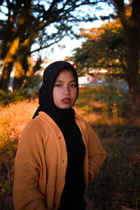 Portrait of young woman standing against trees during autumn