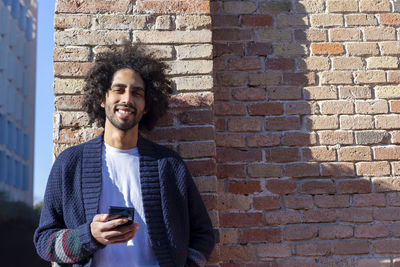 Young man using phone while standing against brick wall