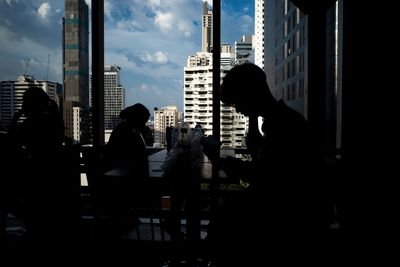 Silhouette people sitting on table by buildings in city