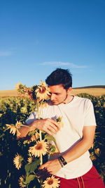 Mid adult man standing amidst flowers against blue sky during sunny day