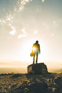 Rear view of man standing on rock against sky during sunset