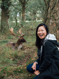 Woman sitting by deer in forest