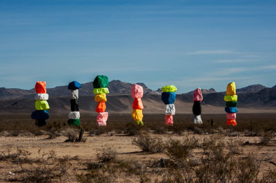 Colorful stacked rocks on field against blue sky