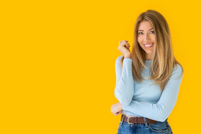 Portrait of young woman standing against yellow background