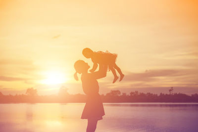 Woman standing by sea against sky during sunset