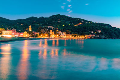 Scenic view of sea by illuminated mountain against sky