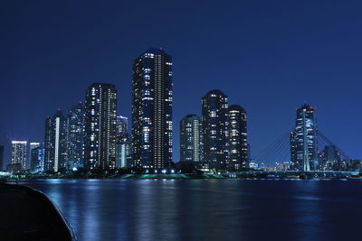 Illuminated modern buildings in city against sky at night