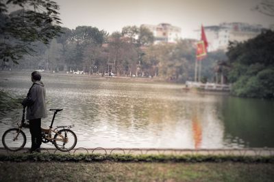 Rear view of man with bicycle standing against lake