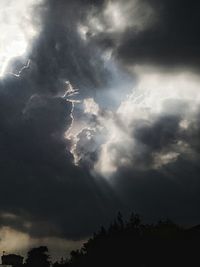 Low angle view of sunlight streaming through clouds