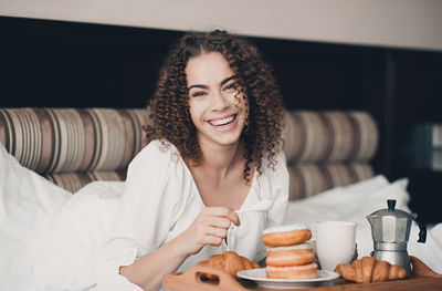 Portrait of smiling woman lying on bed by breakfast