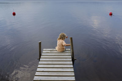 Rear view of woman sitting on pier over lake