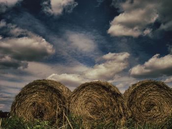 Hay bales on field against cloudy sky