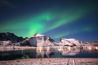 Stunning dancing northern lights over snowy mountains and sea coast in lofoten islands, norway. 