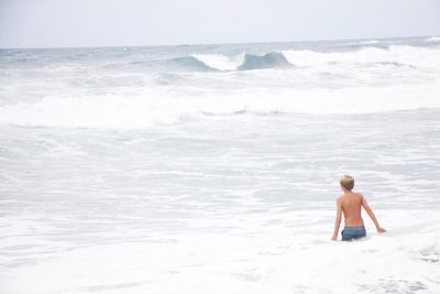 Full length of shirtless boy on beach against sky