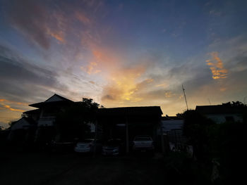 Houses by silhouette buildings against sky during sunset