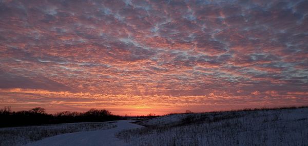 Snow covered field against sky during sunset