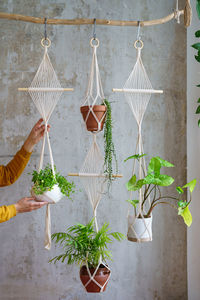 Woman holding macrame plant hanger with houseplants over grey wall at home. hobby, love of plants