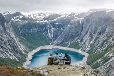 Rear view of people sitting on rock against mountains