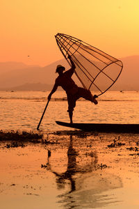 Fisherman fishing in lake with conical fishing nets during sunset