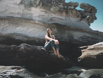 Full length of woman sitting on rock at beach