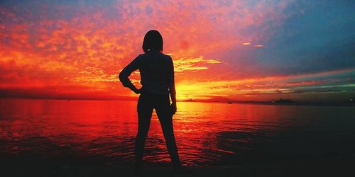 Rear view of silhouette man standing at beach during sunset