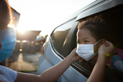 Mother getting daughter dressed with face mask in car