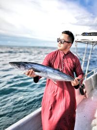 Portrait of man holding fish while standing in boat