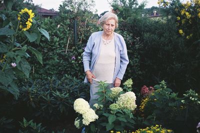 Woman holding umbrella standing by flowering plants