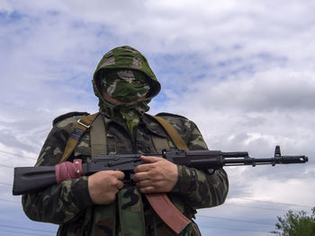 Army soldier holding rifle against cloudy sky