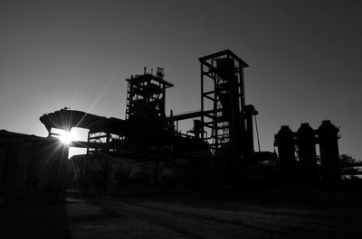 Silhouette factory against clear sky at sunset