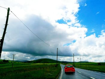 Road passing through field against cloudy sky