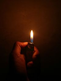 Close-up of hand holding lit candle in darkroom