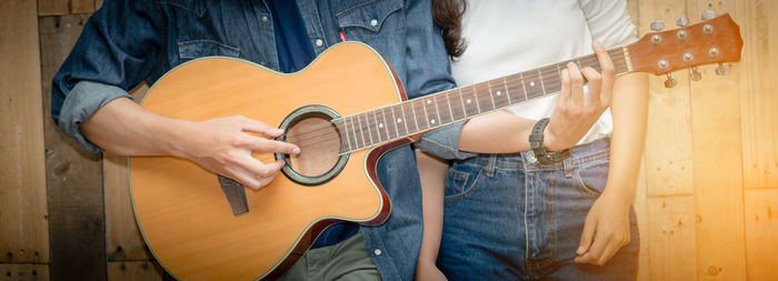 Midsection of man playing guitar by woman standing