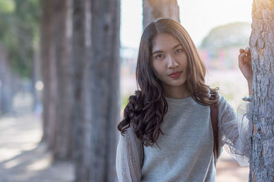 Portrait of young woman standing against tree trunk