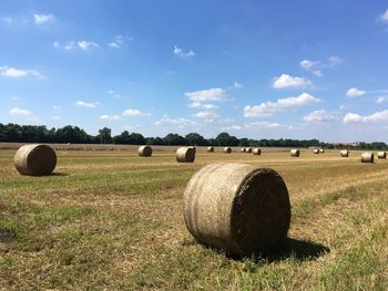 Hay bales on field against blue sky