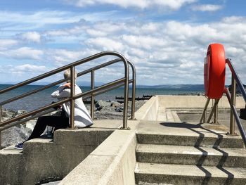 Low section of man on stairs by sea against sky