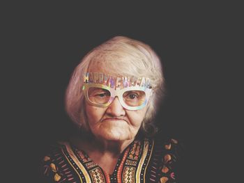 Portrait of senior woman wearing novelty glasses against black background