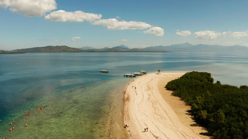 Tropical island and sandy beach with tourists surrounded by coral reef and blue sea in honda bay