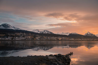 Reflection of buildings and snowcapped mountains in lake during sunset