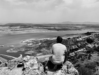 Rear view of man sitting on rock looking at view