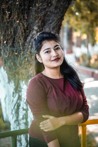 Portrait of smiling woman standing against tree trunk