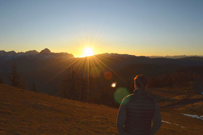 Rear view of woman standing on mountain against sky during sunset