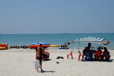 Rear view of people standing on beach against clear sky
