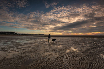 Silhouette people on beach against sky during sunset