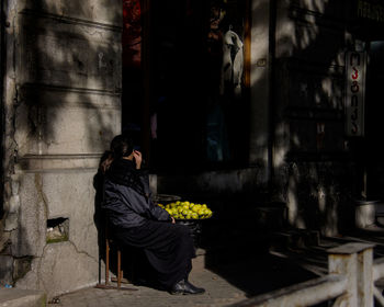 Full length of woman sitting on chair at footpath selling lemons