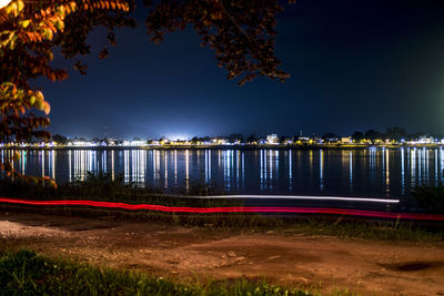 Illuminated city by lake against sky at night