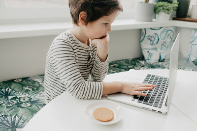 Little boy siting at the kitchen and look at the laptop. high quality photo