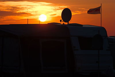 Flag and satellite dish on motor home against sky during sunset