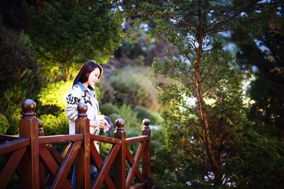 Woman looking down while standing by railing in forest