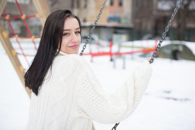 Portrait of young woman swinging in snow covered playground